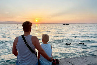 Mother and son watching sunset by the lake with ducks swimming in calm water