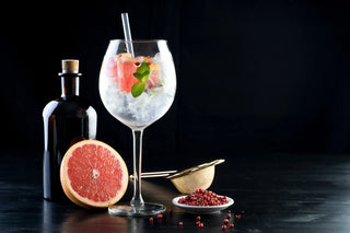 Gin and tonic cocktail with grapefruit, mint, and ice, black bottle, strainer, pink peppercorns