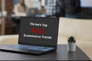 Laptop on table displaying eCommerce trends, modern workspace, small potted plant nearby