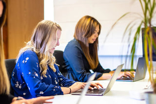 Two women working on laptops in a modern office setting, focusing on website and graphic design tasks.
